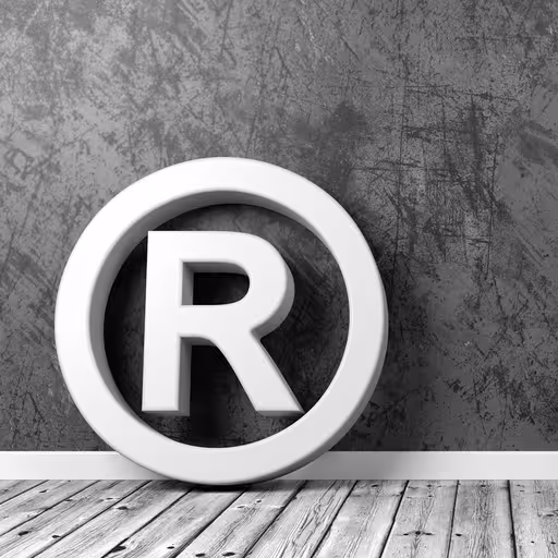 Eine Skulptur in Form eines Warenzeichen-Rs lehnt an einer grauen Wand